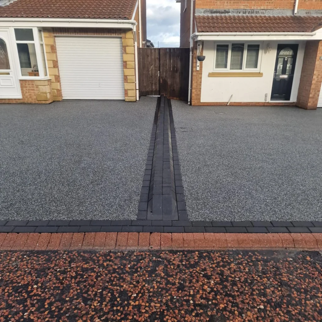 Grey resin-bound driveway with central charcoal block strip between two garages at a Durham property