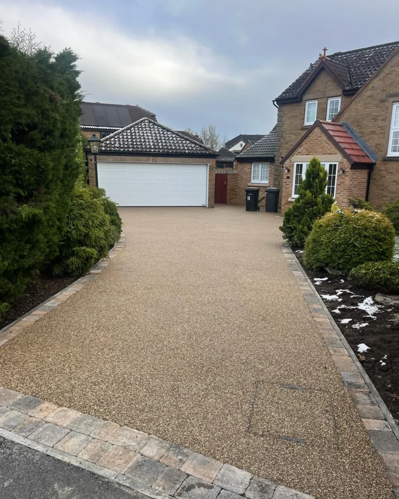 Beige resin-bound driveway with stone block edging leading to a double garage at a Gateshead home