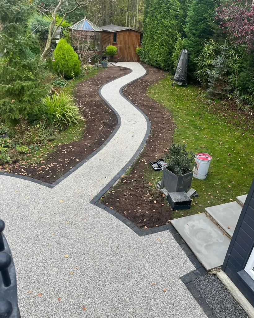 Curving light-grey resin-bound garden path with dark edging winding toward a wooden shed at a Newcastle property