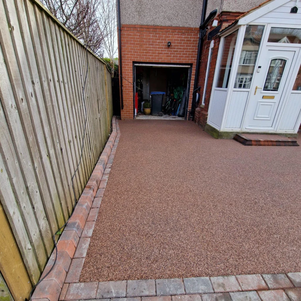 Reddish-brown resin-bound driveway with brick edging leading to garage and porch at a Newcastle home