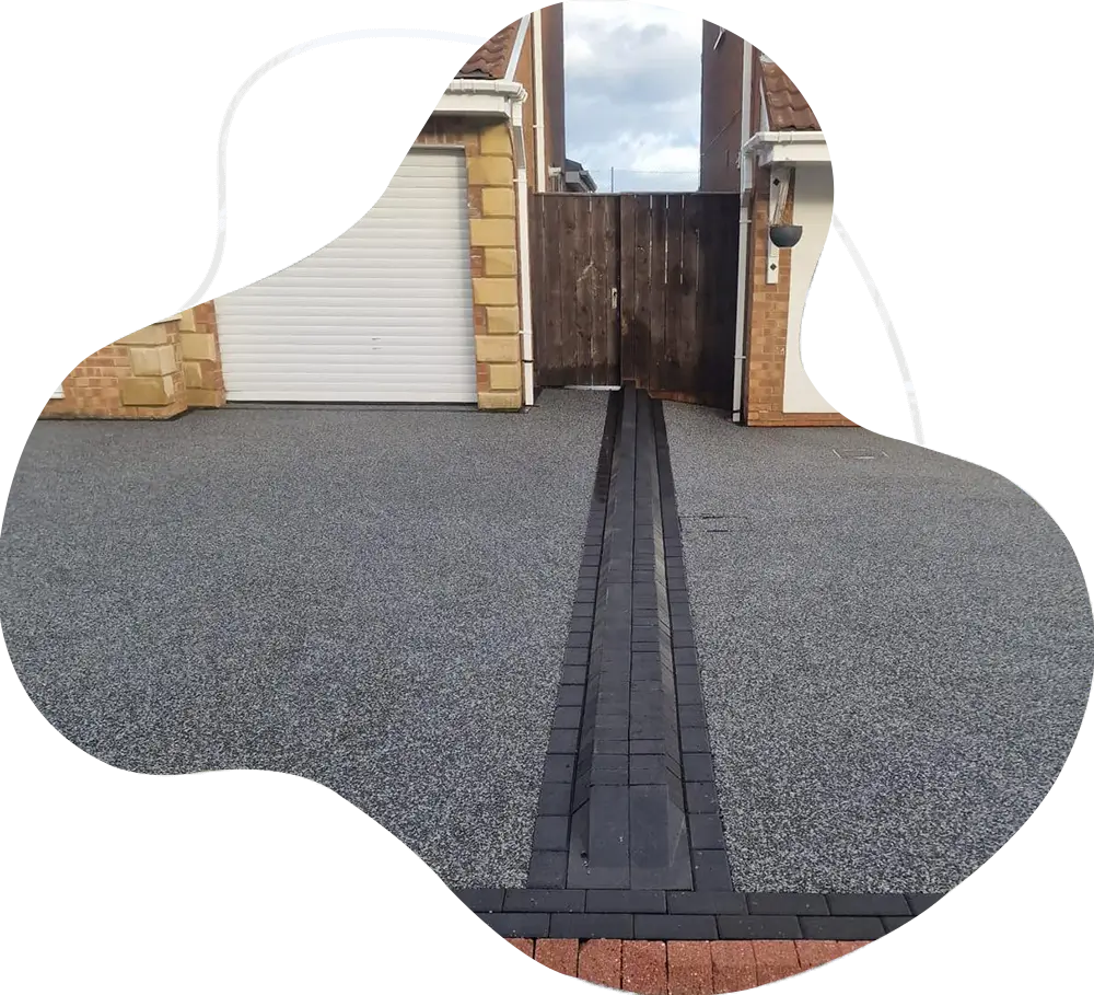 Grey resin-bound driveway with central charcoal block strip meeting a red brick kerb at a Gateshead home